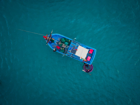 Aerial view of a small blue fishing boat with nets and a solar panel accompanied by a traditional round basket boat floating in the turquoise waters of Vietnam. Aerial view of a small blue fishing boat with nets and a solar panel accompanied by a traditional round basket boat floating in the turquoise waters of Vietnam.