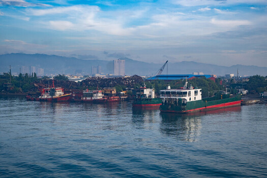 View of cargo ships and vessels docked at the Cebu Port Authority with the city skyline and mountains in the background under a blue sky in Cebu City Central Visayas Philippines. View of cargo ships and vessels docked at the Cebu Port Authority with the city skyline and mountains in the background under a blue sky in Cebu City Central Visayas Philippines.