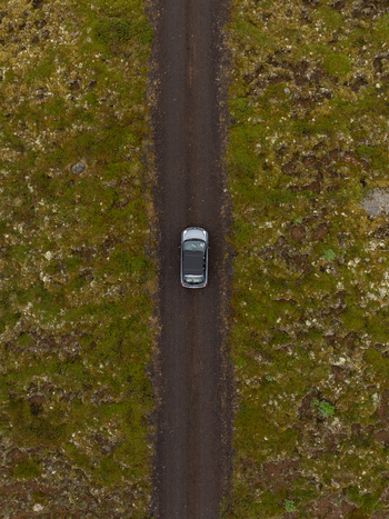 Aerial view of a car driving along a narrow dirt road surrounded by vast mossy volcanic terrain in Raufarhofn Nordurthing Iceland.