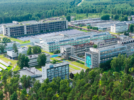 Olaine Latvia 04 July 2026 Aerial view of the industrial complex in Olaine featuring large factory buildings interconnected walkways solar panel arrays and surrounding pine forests.