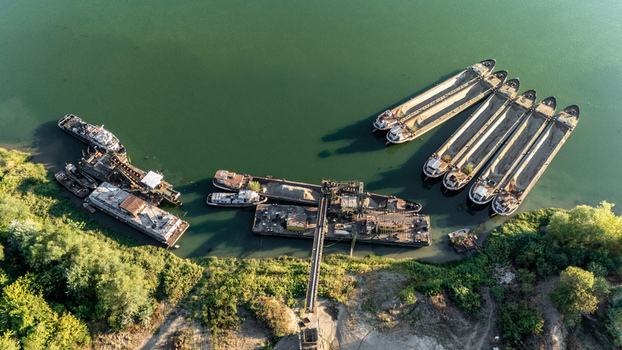 Aerial view of cargo barges moored at an industrial river port with a conveyor system and lush riverbank vegetation in Sremska Mitrovica Vojvodina Serbia.