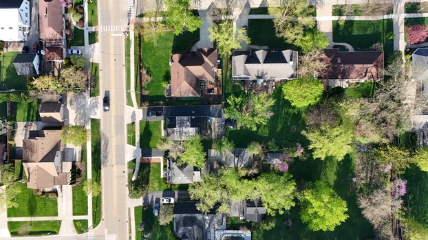 Aerial view of a quiet residential neighborhood with suburban houses green lawns and flowering trees along a straight road. Aerial view of a quiet residential neighborhood with suburban houses green lawns and flowering trees along a straight road.