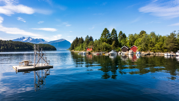 View of a floating wooden platform on a calm fjord with traditional red boathouses and snow capped mountains in Alesund More og Romsdal Norway. View of a floating wooden platform on a calm fjord with traditional red boathouses and snow capped mountains in Alesund More og Romsdal Norway.
