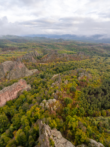 Aerial view of the Belogradchik Rocks featuring unique red sandstone rock formations rising above a dense autumn colored forest under a cloudy sky in Belogradchik Vidin Bulgaria. Aerial view of the Belogradchik Rocks featuring unique red sandstone rock formations rising above a dense autumn colored forest under a cloudy sky in Belogradchik Vidin Bulgaria.