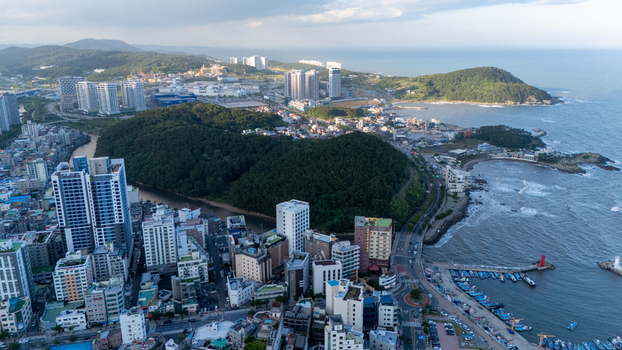 Aerial view of Songjeong dong district in Busan featuring modern high rise buildings a small harbor with fishing boats and lush green hills meeting the sea in Busan South Korea. Aerial view of Songjeong dong district in Busan featuring modern high rise buildings a small harbor with fishing boats and lush green hills meeting the sea in Busan South Korea.