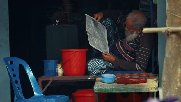 View of an elderly man reading a newspaper in a shop Bangladesh. View of an elderly man reading a newspaper in a shop Bangladesh.