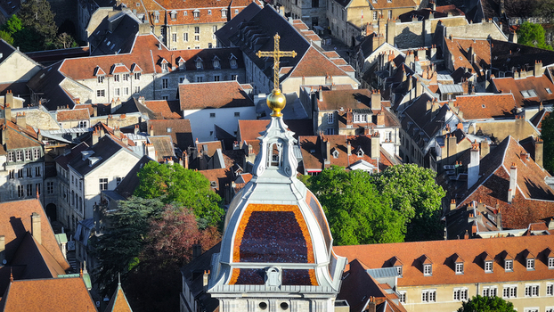 Aerial view of a historic church dome with a golden cross overlooking the red tiled rooftops and stone buildings of the old town in Besancon Bourgogne Franche Comte France. Aerial view of a historic church dome with a golden cross overlooking the red tiled rooftops and stone buildings of the old town in Besancon Bourgogne Franche Comte France.
