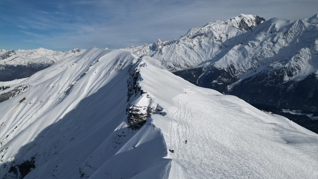 Aerial view of Aiguille Croche mountain ridge covered in snow with skiers on the slopes and the Mont Blanc massif in Les Contamines Montjoie Auvergne Rhone Alpes France. Aerial view of Aiguille Croche mountain ridge covered in snow with skiers on the slopes and the Mont Blanc massif in Les Contamines Montjoie Auvergne Rhone Alpes France.