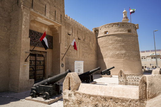 View of Al Fahidi Fort with historic stone walls traditional wooden entrance door and antique cannons displayed in the courtyard in Dubai Dubai United Arab Emirates. View of Al Fahidi Fort with historic stone walls traditional wooden entrance door and antique cannons displayed in the courtyard in Dubai Dubai United Arab Emirates.