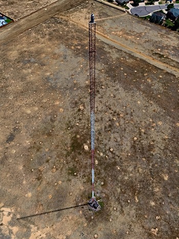 Aerial view of a tall communication tower standing in a dry open field with sparse vegetation and nearby suburban residential streets in Thornton Colorado United States. Aerial view of a tall communication tower standing in a dry open field with sparse vegetation and nearby suburban residential streets in Thornton Colorado United States.