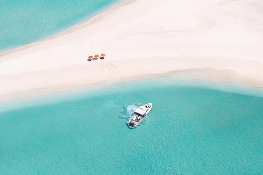 Aerial view of a white sandbank with red umbrellas and a boat in turquoise waters Vashafaru Haa Alif Atoll Maldives. Aerial view of a white sandbank with red umbrellas and a boat in turquoise waters Vashafaru Haa Alif Atoll Maldives.