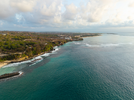 Aerial view of the Hilton Bali Resort coastline featuring turquoise waters waves breaking on the reef and lush green vegetation along the cliffs in Kecamatan Kuta Selatan Bali Indonesia. Aerial view of the Hilton Bali Resort coastline featuring turquoise waters waves breaking on the reef and lush green vegetation along the cliffs in Kecamatan Kuta Selatan Bali Indonesia.