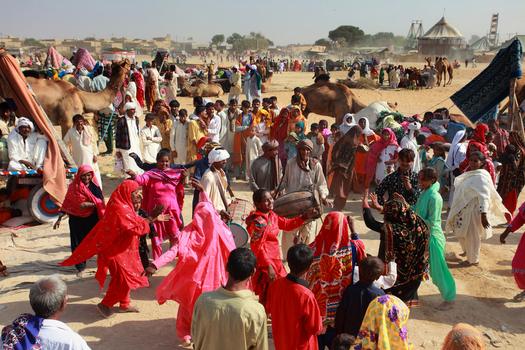 View of the Chanan Pir festival in the desert with people dancing in traditional clothing camels and musical instruments in Yazman Punjab Pakistan.
