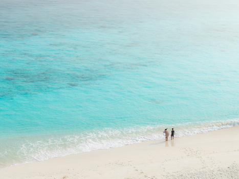 Aerial view of a pristine white sandy beach kissed by vibrant turquoise waves as two figures stand at the tranquil water s edge Hoarafushi Thiladhunmathee Uthuruburi Maldives. Aerial view of a pristine white sandy beach kissed by vibrant turquoise waves as two figures stand at the tranquil water s edge Hoarafushi Thiladhunmathee Uthuruburi Maldives.