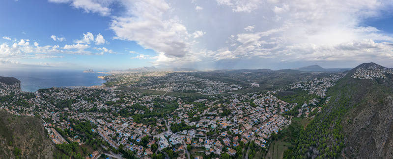 Aerial view of the coastal town of Moraira featuring residential areas lush greenery and the Mediterranean Sea under a cloudy sky in Moraira Valencian Community Spain.