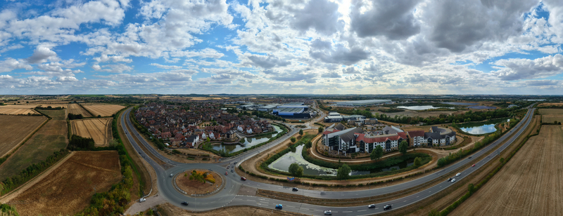 Aerial view of Wixams Retirement Village with unique architecture surrounded by green spaces a small lake and nearby residential areas in Bedford England United Kingdom.