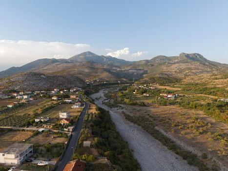 Aerial view of the Kir riverbed winding through the rural landscape with scattered houses olive groves and distant mountains in Boks Qarku i Shkodres Albania.