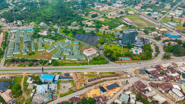 Aerial view of a modern cylindrical office building a hospital complex with green roofs a tennis court and surrounding urban infrastructure in Uyo Akwa Ibom Nigeria. Aerial view of a modern cylindrical office building a hospital complex with green roofs a tennis court and surrounding urban infrastructure in Uyo Akwa Ibom Nigeria.