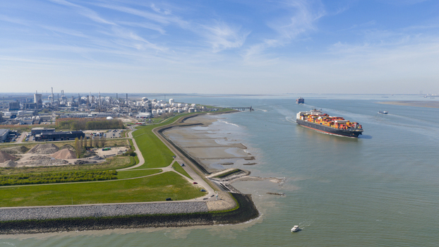 Terneuzen Netherlands 08 April 2026 Aerial view of a large container ship navigating the Westerschelde river past the industrial port area and green dikes under a clear blue sky. Terneuzen Netherlands 08 April 2026 Aerial view of a large container ship navigating the Westerschelde river past the industrial port area and green dikes under a clear blue sky.