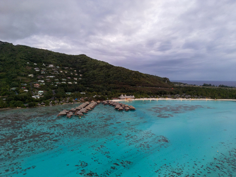 Aerial view of Sofitel Kia Ora Moorea Beach Resort with overwater bungalows in a turquoise lagoon lush green mountains and cloudy sky in Moorea Maiao Windward Islands French Polynesia. Aerial view of Sofitel Kia Ora Moorea Beach Resort with overwater bungalows in a turquoise lagoon lush green mountains and cloudy sky in Moorea Maiao Windward Islands French Polynesia.