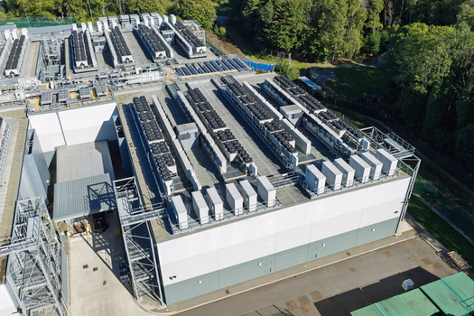 Aerial view of a large data center facility with rows of cooling units on the roof surrounded by trees and paved areas United Kingdom.