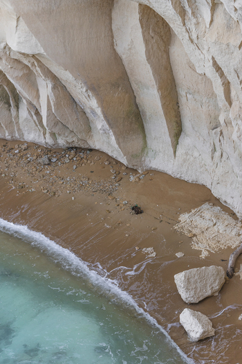 View of a secluded sandy beach nestled beneath towering white limestone cliffs and turquoise sea waves in Syracuse Sicily Italy.