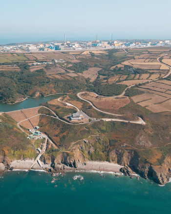 Aerial view of the rugged coastline and agricultural fields of La Hague with the nuclear power plant in the distance La Hague Normandie France.