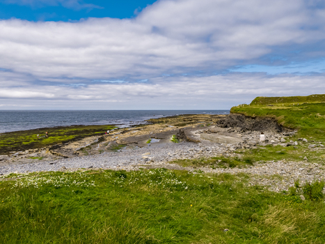 Aerial view of Storm Beach with rocky coastline green grassy cliffs and the Atlantic Ocean under a cloudy blue sky in Carrownedin County Sligo Ireland.