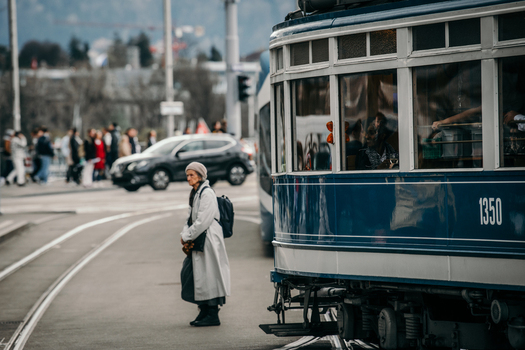 Zurich Switzerland 02 April 2023 View of a woman clad in a light coat amidst the city s pulse standing near a tram with blurred cars and people in background. Zurich Switzerland 02 April 2023 View of a woman clad in a light coat amidst the city s pulse standing near a tram with blurred cars and people in background.