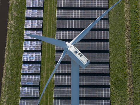 Aerial view of a white wind turbine and rows of photovoltaic solar panels on a green meadow under bright sunlight in the Netherlands. Aerial view of a white wind turbine and rows of photovoltaic solar panels on a green meadow under bright sunlight in the Netherlands.