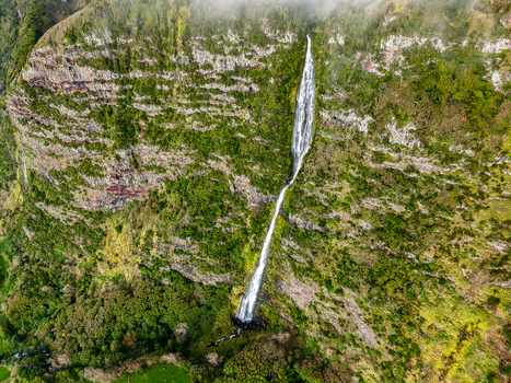 Aerial view of a majestic waterfall cascading down the rugged verdant cliffs a ribbon of white against the deep green Faj&atilde; Grande Azores Portugal.