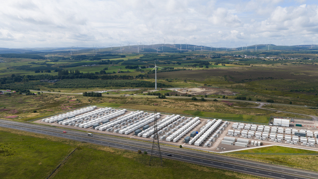 Aerial view of the large scale battery energy storage system in Coalburn featuring rows of white containers wind turbines and rolling green hills Coalburn Scotland United Kingdom.