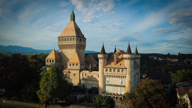 Aerial view of the historic Vufflens le Chateau castle featuring its massive central keep and pointed turrets under a soft blue sky Vufflens le Chateau Vaud Switzerland. Aerial view of the historic Vufflens le Chateau castle featuring its massive central keep and pointed turrets under a soft blue sky Vufflens le Chateau Vaud Switzerland.