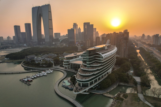 Aerial view of the ship shaped Crowne Plaza Suzhou and the Gate to the East skyscraper at sunset over the Jinji Lake waterfront with boats at the pier in Suzhou Jiangsu China. Aerial view of the ship shaped Crowne Plaza Suzhou and the Gate to the East skyscraper at sunset over the Jinji Lake waterfront with boats at the pier in Suzhou Jiangsu China.