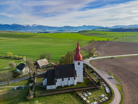Aerial view of the historic Church of St. Ladislaus with its red steeple and fortified wall surrounded by green fields and the Tatra Mountains Liptovske Matiasovce Zilina Region Slovakia.