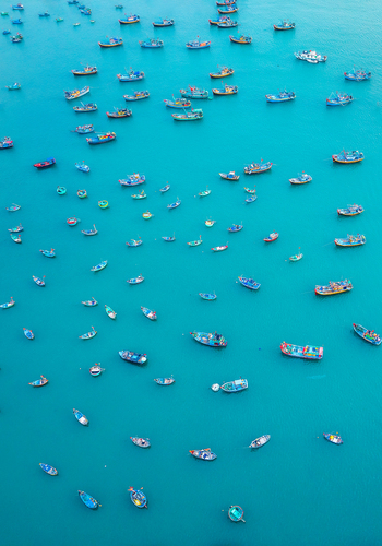 Aerial view of numerous colorful fishing boats scattered across the calm turquoise waters of the sea in Vietnam. Aerial view of numerous colorful fishing boats scattered across the calm turquoise waters of the sea in Vietnam.