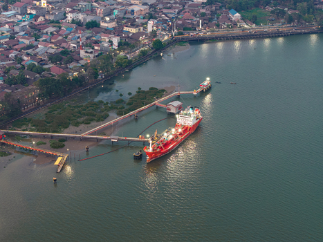 Aerial view of a large red tanker ship docked at an industrial pier on the Mahakam River with urban rooftops and riverside infrastructure in Samarinda East Kalimantan Indonesia. Aerial view of a large red tanker ship docked at an industrial pier on the Mahakam River with urban rooftops and riverside infrastructure in Samarinda East Kalimantan Indonesia.