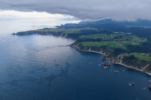 Aerial view of the rugged coastline near Silence Beach Viewpoint with steep cliffs green meadows and small villages under a cloudy sky in Cudillero Asturias Spain.