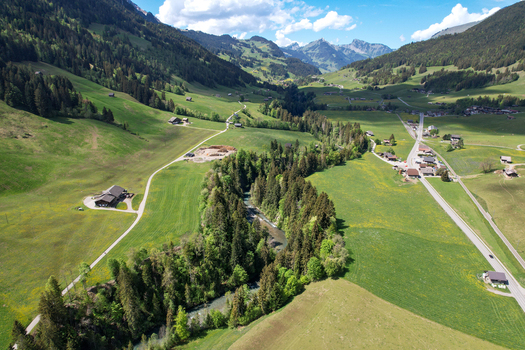 Aerial view of the Sarine river winding through lush green meadows and traditional chalets in the alpine valley of Rougemont Vaud Switzerland. Aerial view of the Sarine river winding through lush green meadows and traditional chalets in the alpine valley of Rougemont Vaud Switzerland.