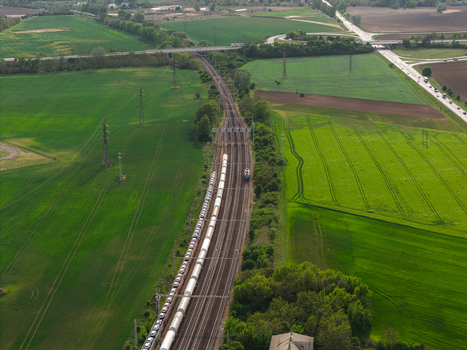 Aerial view of a long freight train transporting white tanks along railway tracks through lush green fields and rural landscape Hrusky South Moravian Region Czechia. Aerial view of a long freight train transporting white tanks along railway tracks through lush green fields and rural landscape Hrusky South Moravian Region Czechia.