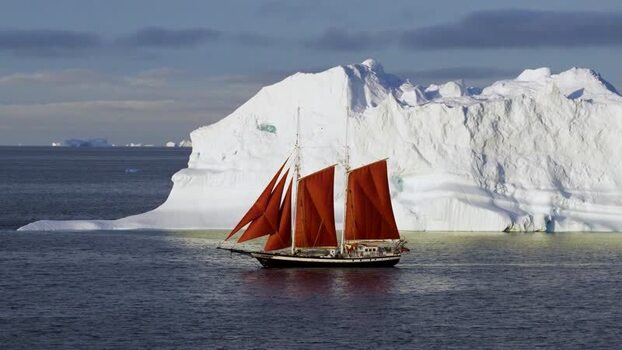 Aerial view of a sailboat with red sails near an iceberg Greenland. Aerial view of a sailboat with red sails near an iceberg Greenland.