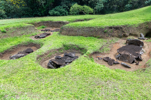 View of the ancient stone burial sites at San Agustin Archaeological Park featuring grassy mounds and historic stone structures San Agustin Huila Colombia.