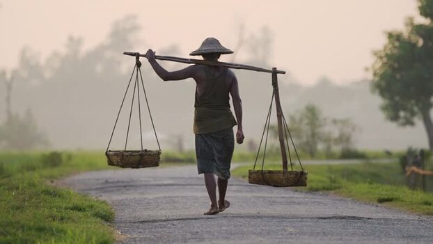 View of a man carrying baskets on a yoke in Bogura Bangladesh.