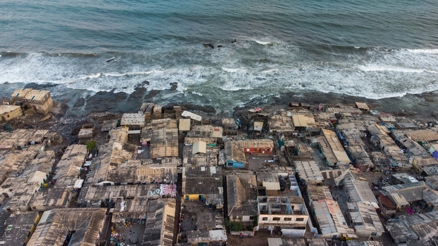 Aerial view of Teshie coastal settlement with dense housing and corrugated metal roofs along the rocky shoreline of the Atlantic Ocean in Accra Greater Accra Region Ghana.