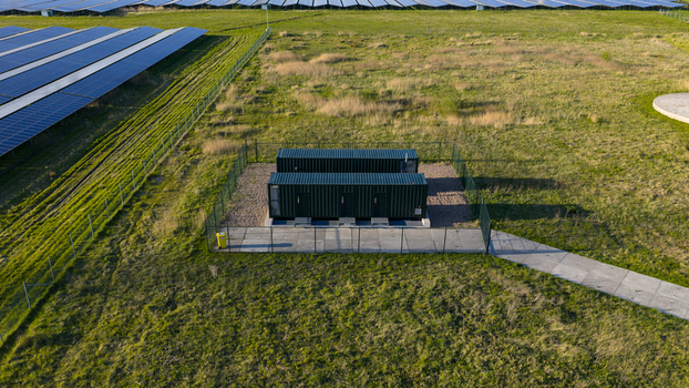 Aerial view of two green industrial containers in a fenced enclosure next to a large solar panel array in a green field Farmsum Groningen Netherlands.