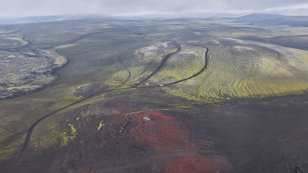 Aerial view of Landmannalaugar featuring vibrant moss covered hills dark volcanic lava fields patches of red soil and a winding dirt road Hella Rangarthing ytra Iceland. Aerial view of Landmannalaugar featuring vibrant moss covered hills dark volcanic lava fields patches of red soil and a winding dirt road Hella Rangarthing ytra Iceland.