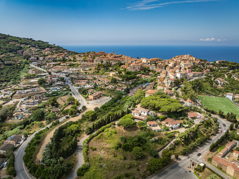Aerial view of the historic town of Capoliveri nestled on a hillside with Mediterranean vegetation winding roads and a soccer field in Capoliveri Tuscany Italy.