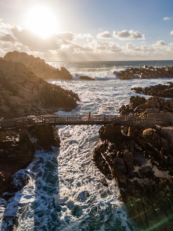 Aerial view of Canal Rocks Bridge spanning rugged rock formations with a person walking across surrounded by crashing waves in Yallingup Western Australia Australia. Aerial view of Canal Rocks Bridge spanning rugged rock formations with a person walking across surrounded by crashing waves in Yallingup Western Australia Australia.