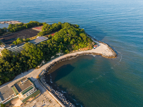 Aerial view of the coastline in Kiten featuring a rocky breakwater lush green forest a sports field and buildings along the Black Sea shore in Kiten Burgas Bulgaria. Aerial view of the coastline in Kiten featuring a rocky breakwater lush green forest a sports field and buildings along the Black Sea shore in Kiten Burgas Bulgaria.