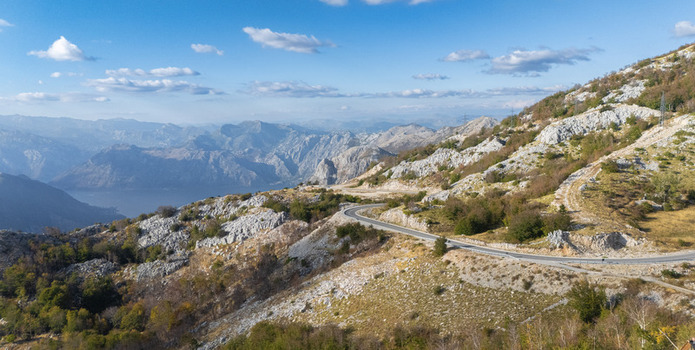 Aerial view of a winding mountain road cutting through the rugged rocky landscape with distant mountains and a clear blue sky in Tivat Tivat Municipality Montenegro. Aerial view of a winding mountain road cutting through the rugged rocky landscape with distant mountains and a clear blue sky in Tivat Tivat Municipality Montenegro.